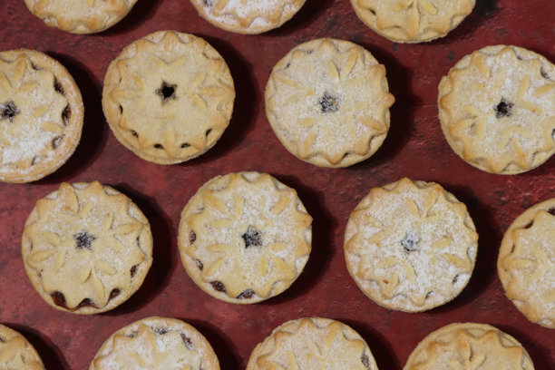 全画幅图像，展示了手工制作的肉馅饼的排列表，顶部有酥皮雪花状的盖子，节日圣诞甜点，酥皮糕点配甜肉馅，撒上糖粉，斑驳的红色背景，俯视角度。图片下载