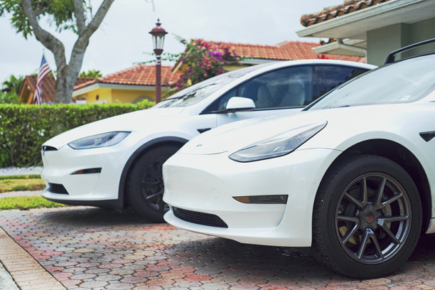 美国佛罗里达州迈阿密 - 2025年5月3日：两辆白色特斯拉汽车的局部特写。前景中的Model 3展示了其时尚、空气动力学的外观，包括车头灯、前脸和合金轮毂。图片下载