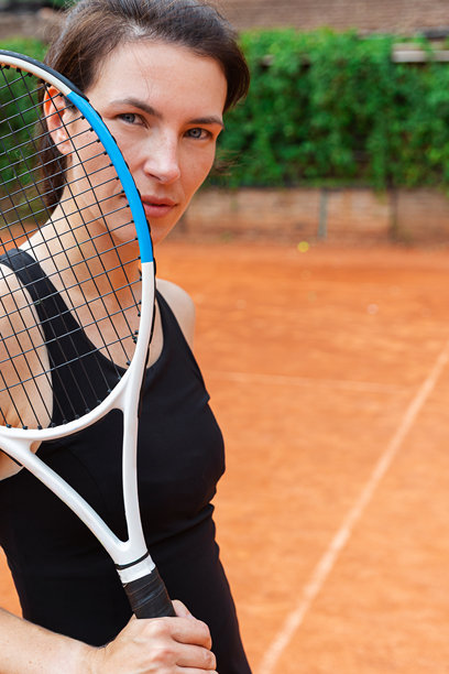 一名女子在红土球场上握着网球拍。照片通过体育精神和对成就的奉献，展现了专注、自信和个人力量。图片下载