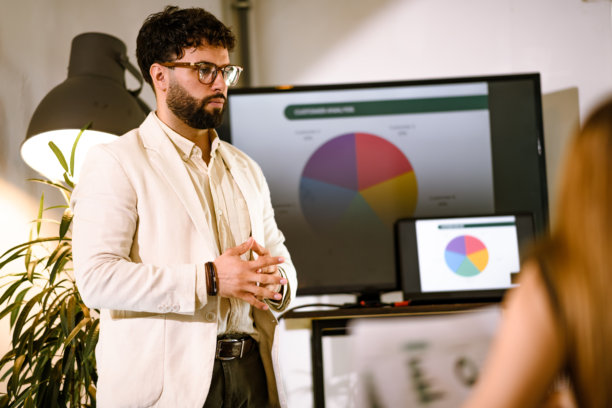 一位年轻的专业人士在现代工作空间进行商务演示，公司会议期间屏幕上投影着图表。图片下载