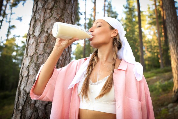 牛奶广告。女孩在自然背景下拿着一瓶牛奶。健康饮食和自我关怀。高质量照片图片下载