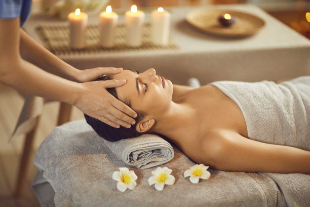 特写照片：一位漂亮的年轻女子闭着眼睛，在水疗中心接受面部或头部按摩。图片下载