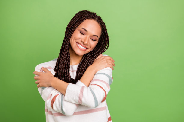 照片：快乐迷人的黑皮肤女子拥抱自己，心情愉悦，背景为绿色图片下载