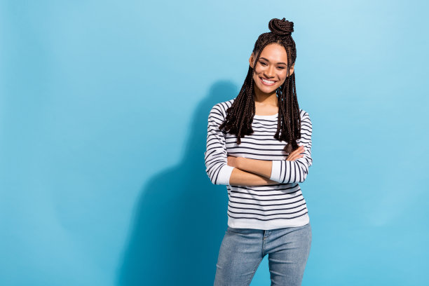 照片：年轻的非洲女孩，快乐积极的微笑，自信地双手交叉，在蓝色的背景下图片下载