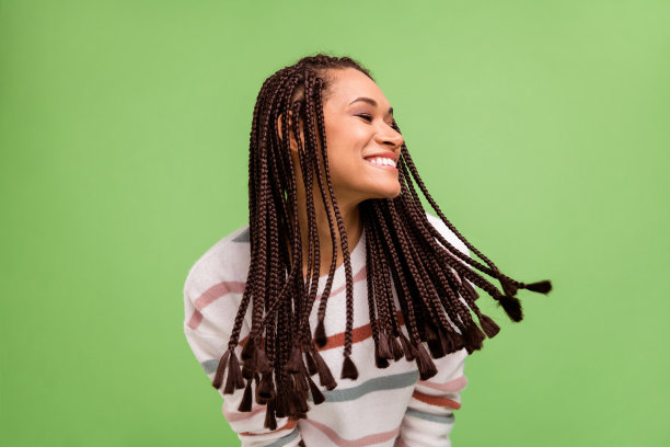 照片：一位心情愉悦、头发飞扬的非裔美国年轻女子，在绿色背景下展露灿烂笑容图片下载