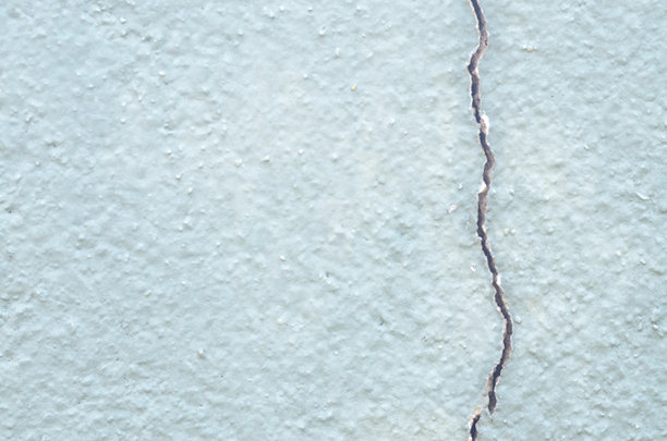 裂缝墙壁的细节照片，其纹理表面被一道深邃的裂缝撕裂，象征着岁月、衰败和崩塌。图片下载