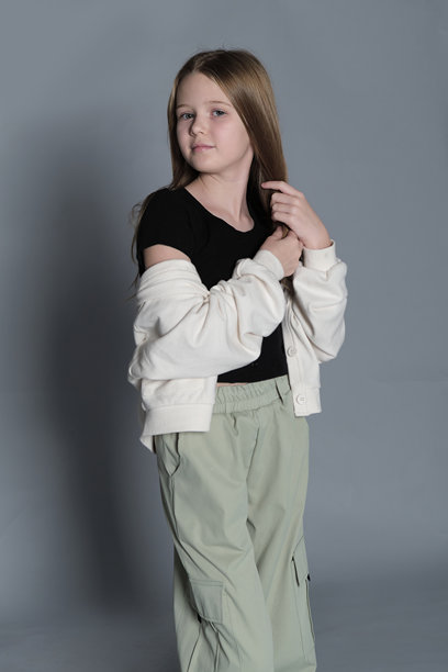 身穿黑色上衣和绿色裤子的年轻女孩双手合十而立，若有所思地看向别处。这张图片突显了孩子们的沉思特质，捕捉了一个宁静而内省的瞬间。图片下载