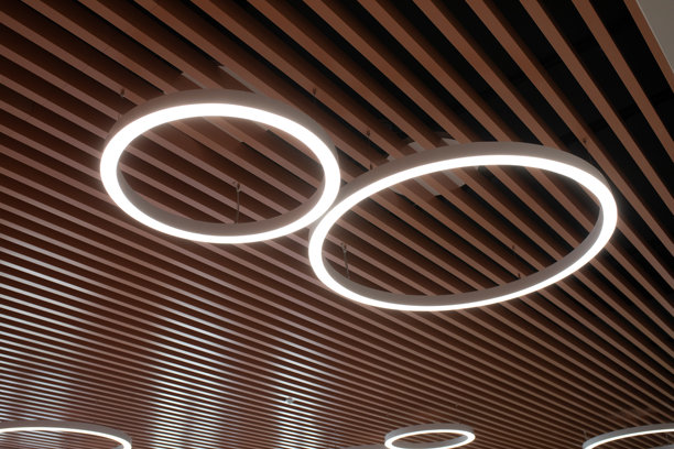 木质格栅天花板上的现代圆形LED灯。办公室或公共空间的优雅、未来感照明设计。照片图片下载