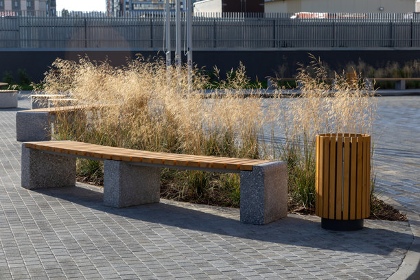 长椅和垃圾桶旁边的蒲公英景观。带有混凝土底座和木制座椅的实用城市家具，用于公共休息区。照片图片下载