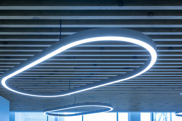 木制格栅天花板上的椭圆形LED灯具。现代吊灯，带有蓝色光晕，适用于办公室或公共照明。时尚的室内照明，为现代建筑设计。照片图片下载