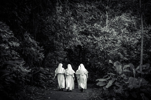三位身着白色道袍的修女在林间小径上行走（黑白照片）图片下载