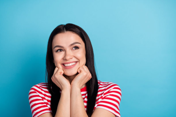 照片：一位快乐、微笑、梦幻、迷人的女性，带着 the copyspace，在蓝色背景前深情地遐想，孤立。图片下载