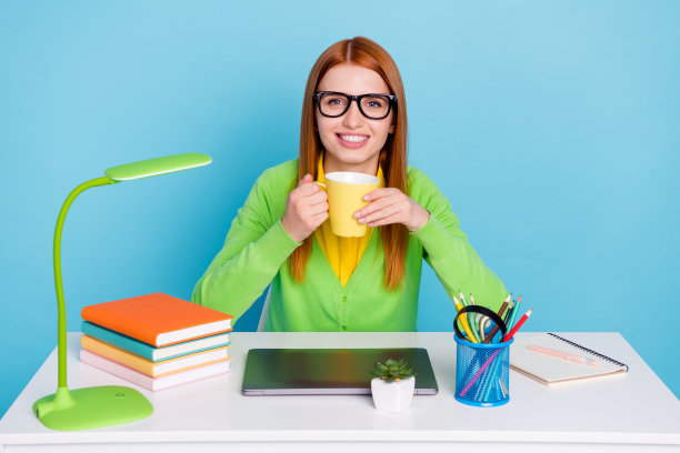 穿着绿色毛衣、戴着眼镜的年轻女士在蓝色背景下喝茶的照片图片下载