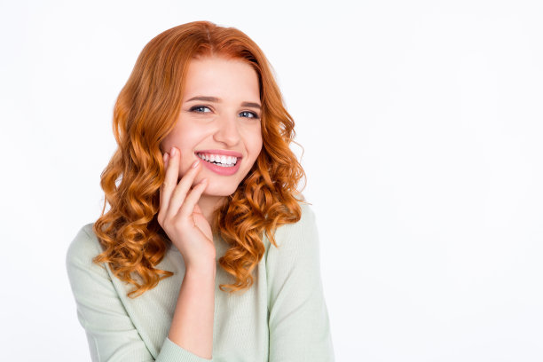 照片肖像：一位留着红发的年轻女子穿着休闲装，双手触碰着脸颊，面带微笑，背景为纯白色，留有复制空间。图片下载