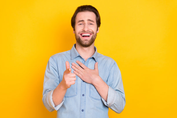 一个年轻男人大笑并用手指着你，在明亮的黄色背景上，这是一个有趣的笑话，照片肖像，孤立。图片下载