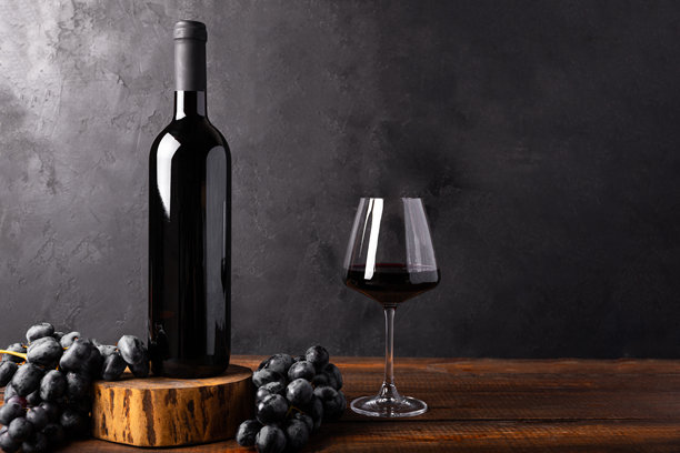 红酒瓶和酒杯，搭配旧木头和葡萄。简约构图，黑色背景，适用于产品品牌、形象和包装。留有复制空间。图片下载