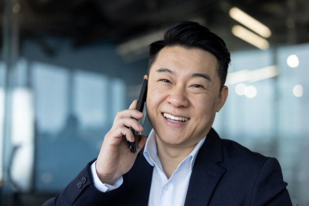 特写照片，一位年轻的微笑的亚洲商人在办公室里打电话，并看向镜头图片下载