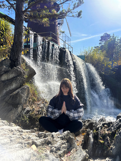 白种女人在瀑布旁的自然环境中冥想，双手合十。竖幅照片图片下载