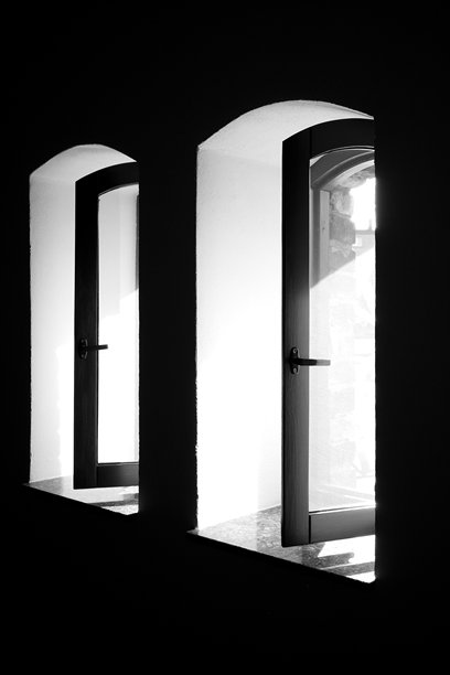 黑色和白色照片，展示了黑暗室内带有敞开窗框的拱形窗户。极简主义建筑构图，具有强烈的光影对比。图片下载