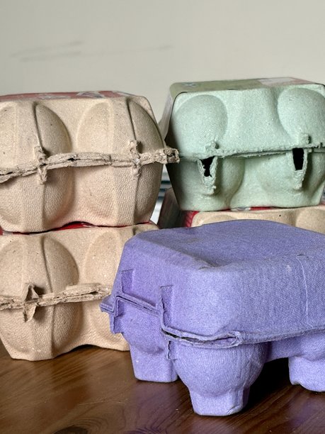 彩色的、环保的回收纸浆蛋盒堆叠在木桌上。图片在自然光下展示了各种颜色的蛋盒，彰显了可持续性。图片下载