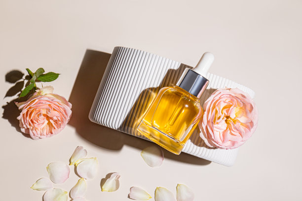 滴管式玻璃瓶装有用于面部护肤的天然精油或精华，放置在带有玫瑰的浮雕讲台上。空白瓶子模型，俯视角度。图片下载