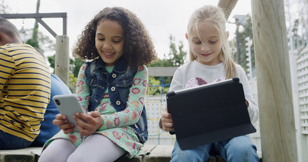朋友、女孩们在花园里带着科技产品开心地对着镜头微笑，用于社交媒体，在后院享受乐趣和休息。孩子们在公园里一起玩耍，通过手机、平板电脑和网络建立联系，度过假期，玩游戏或看表情包。图片下载