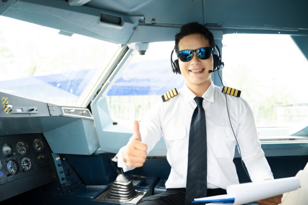 身着制服、戴着耳机的航空公司飞行员在飞机驾驶舱内竖起大拇指，非常适合航空、旅行和专业航空生活方式的素材图。图片下载