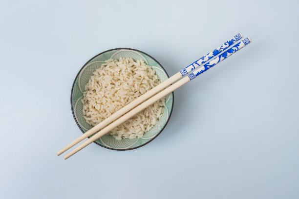 俯视角度的图片，展示了一个斜放的绿松石蓝米饭碗、带有青金石蓝图案的筷子以及青色背景。图片下载