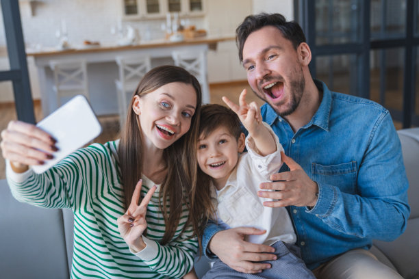 白种人一家人在沙发上开心地自拍，在家中放松，使用社交媒体、观看流媒体，并带着承诺创造美好回忆。照片中洋溢着笑容，分享动态，充满爱、关怀与信任，人们在舒适的公寓里。图片下载