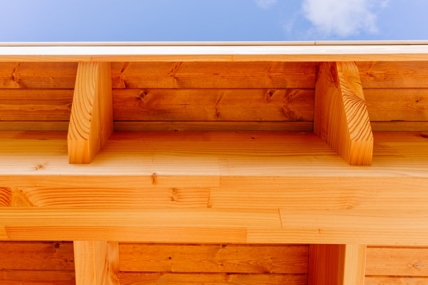 蓝天下木质屋顶梁和悬挑结构的特写。照片展示了天然木材纹理和现代建筑细节。图片下载