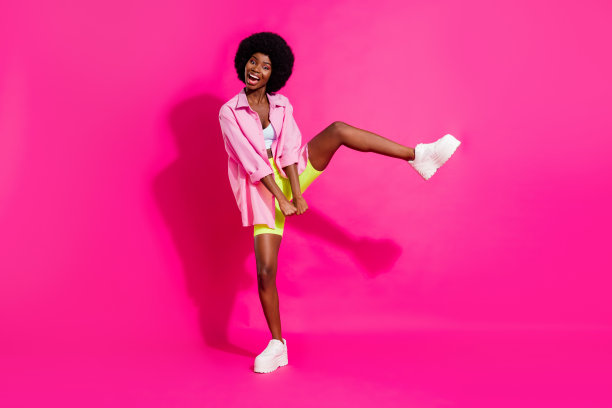 照片：一位身穿露脐上衣、黑色皮肤、面带笑容、跳着舞的可爱女性，背景为粉色。图片下载