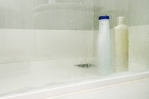 玻璃淋浴房内放着几个塑料洗发水瓶，上面有水滴和一个白色盘子图片下载
