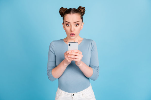 照片：一个害怕、担心的年轻女孩，犯了错误后在评论区发帖，手持手机，孤立在蓝色背景上图片下载