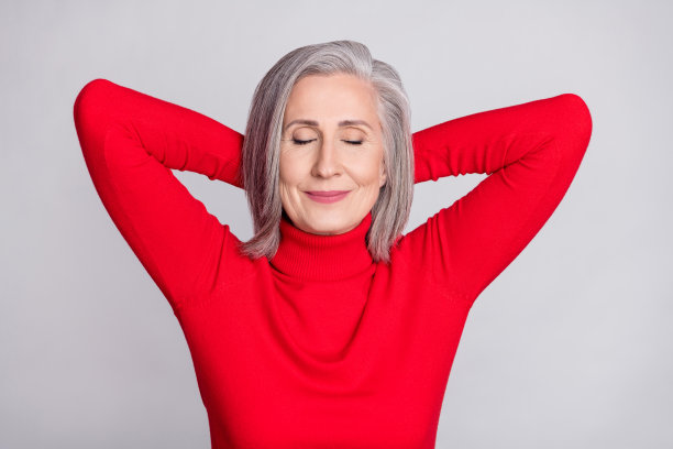 俯视角度拍摄的年长女性照片，她快乐地微笑着，在灰色背景下双手枕在头后安详入睡图片下载