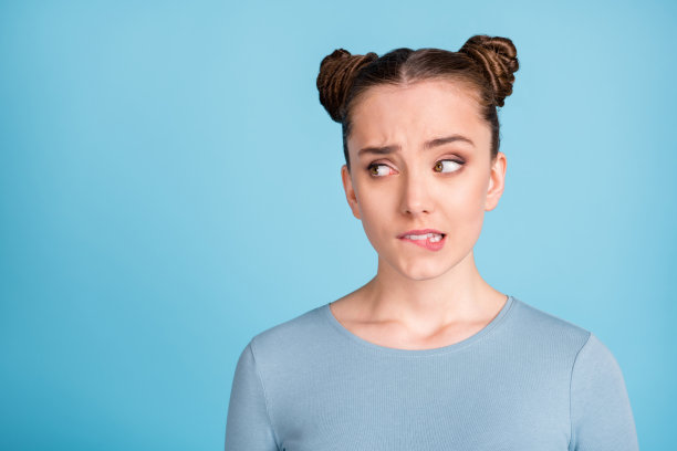 照片：一位不开心、犹豫的年轻女子，眼神空洞，咬着嘴唇，孤立在粉蓝色背景上。图片下载