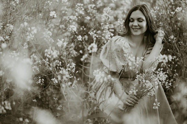 黑白照片中身穿复古风格的年轻女子坐在油菜花田中图片下载