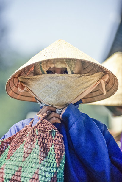 扫描的彩色历史照片，摄于1995年3月3日，越南顺化，一位戴着斗笠和防尘口罩、面容模糊的年轻女子。图片下载