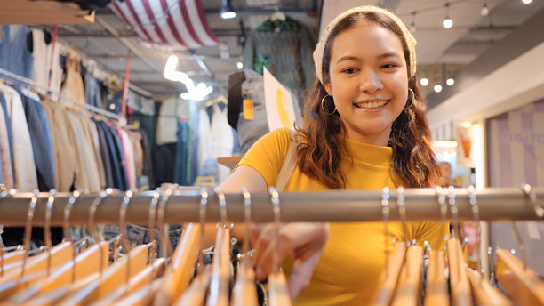 年轻的Z世代亚洲女性游客，在零浪费、环保的二手商店或跳蚤市场里，挑选复古风格的织物。一位快乐的亚洲女性在小型零售店里。图片下载