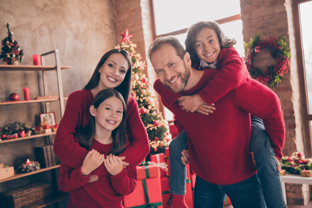 照片：温馨有爱的家庭在装饰一新的圣诞家居室内，享受平安夜，爸爸背着儿子玩耍图片下载