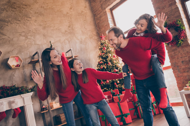 照片：在一个装饰过的圣诞节室内家中，一对友善积极的父子，父亲背着儿子，两人一起挥手。图片下载