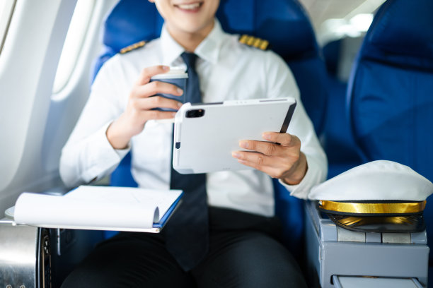 自信的飞行员身着制服，在飞机客舱中使用智能手机，非常适合航空、通信和旅行生活方式的图片素材。图片下载