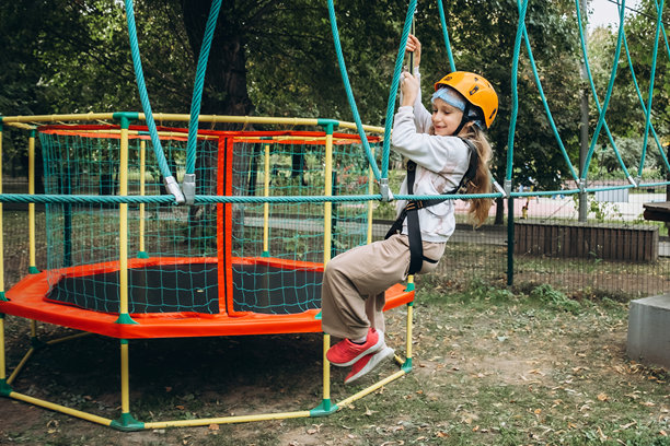 一个穿着安全装备的幼儿在冒险公园的挑战性绳索课程中前进。这张照片捕捉了在郁郁葱葱的环境中进行这项户外活动时的专注和决心。图片下载