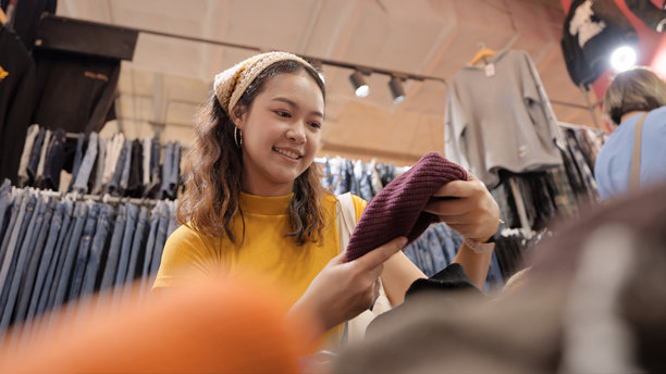 年轻的Z世代亚洲女游客在零浪费环保商店里挑选商品，该商店出售二手商品、跳蚤市场和复古风格的布料。快乐的亚洲女性在小型零售店里。图片下载