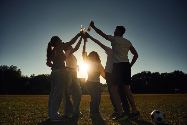 逆光拍摄。人们欢呼庆祝，手持啤酒瓶的黑暗照片。图片下载