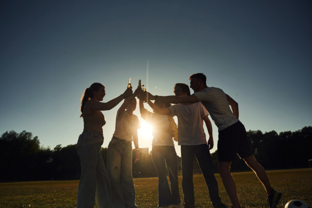 逆光拍摄。人们欢呼庆祝、举着啤酒瓶的黑暗照片图片下载