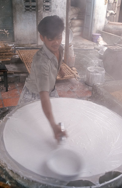 越南工人于1992年10月15日在西贡（越南）将煮沸的米浆摊在布上制作米粉的历史彩色照片图片下载