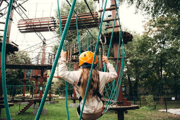 一个穿着安全装备的幼儿在探险公园的挑战性绳索课程中前行。这张照片捕捉了在郁郁葱葱的环境中进行户外活动时的专注和决心。图片下载