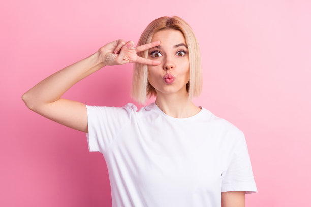 年轻女孩嘟着嘴，送出飞吻，比出象征和平的V字手势，在粉彩背景下显得很酷。图片下载