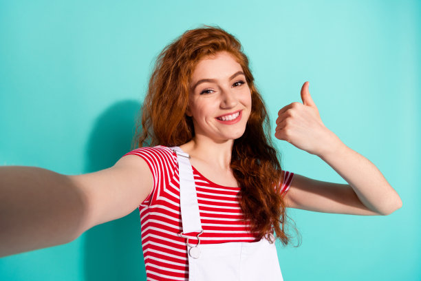 面带微笑、竖起大拇指的迷人女孩的自画像，展现出酷炫、信任和完美，在鲜艳的蓝色背景下独立突出图片下载