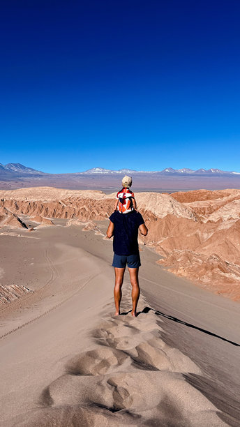 垂直照片，一位无法辨认的游客游客将儿子或蹒跚学步的孩子扛在肩上，站在沙丘顶上图片下载